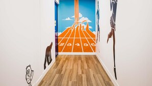 Un pasillo con suelo de madera, una pared azul con un mural de circuito de carreras y otra pared blanca con un adhesivo de un búho negro.