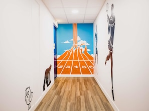 A hallway with a wooden floor, a blue wall with a number race track mural, and a white wall with a black owl decal.