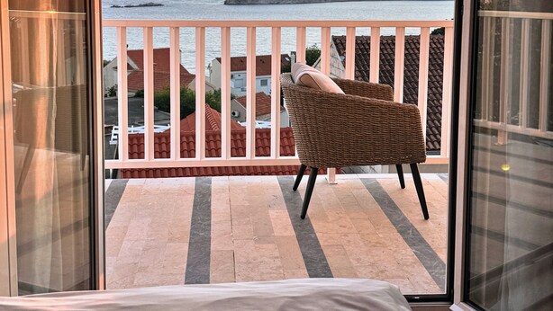 Ein Balkon mit Korbstuhl, Bett und Blick auf das Meer bei Sonnenuntergang.