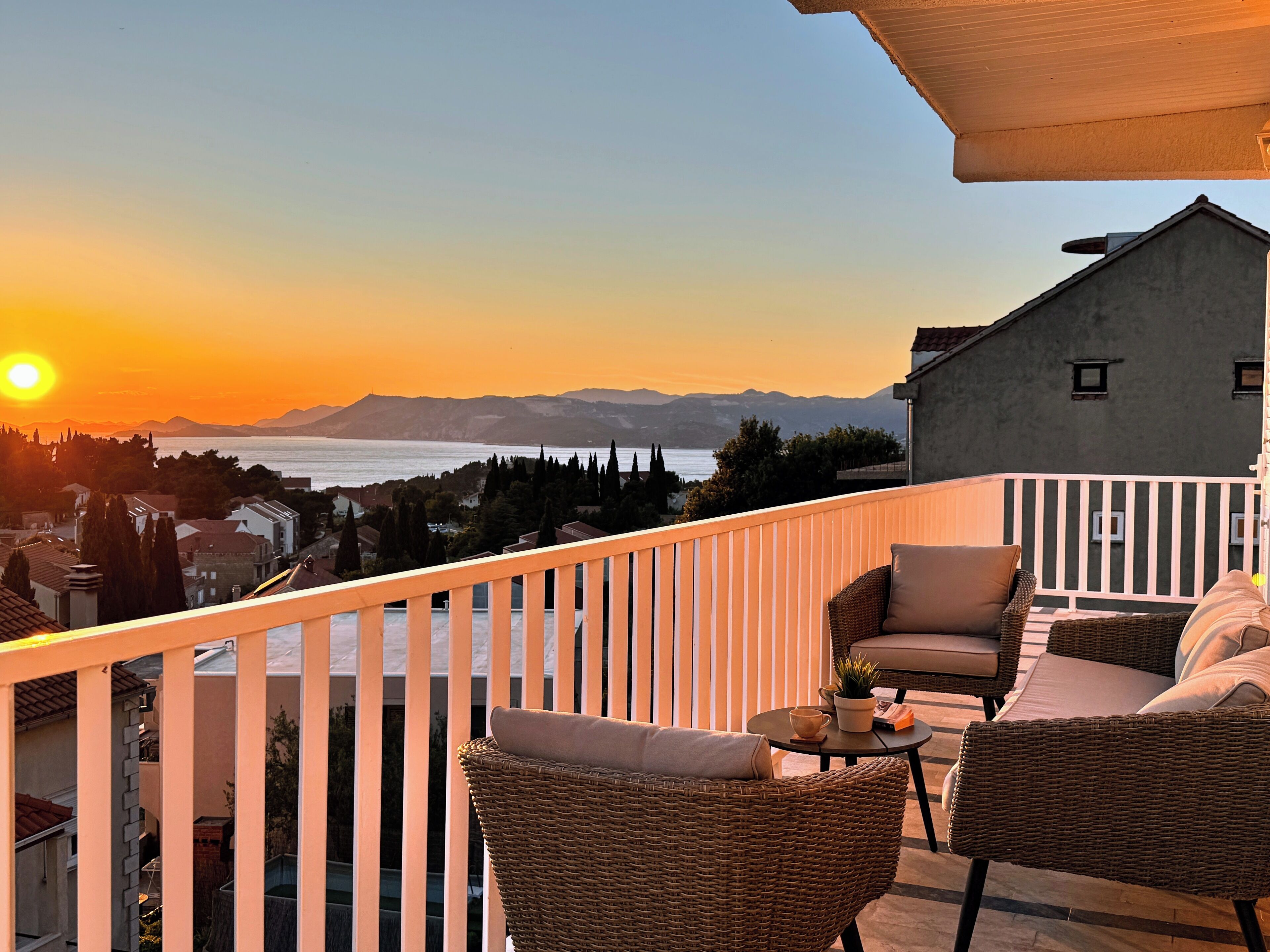 A balcony with wicker furniture and a view of the sunset over the sea.