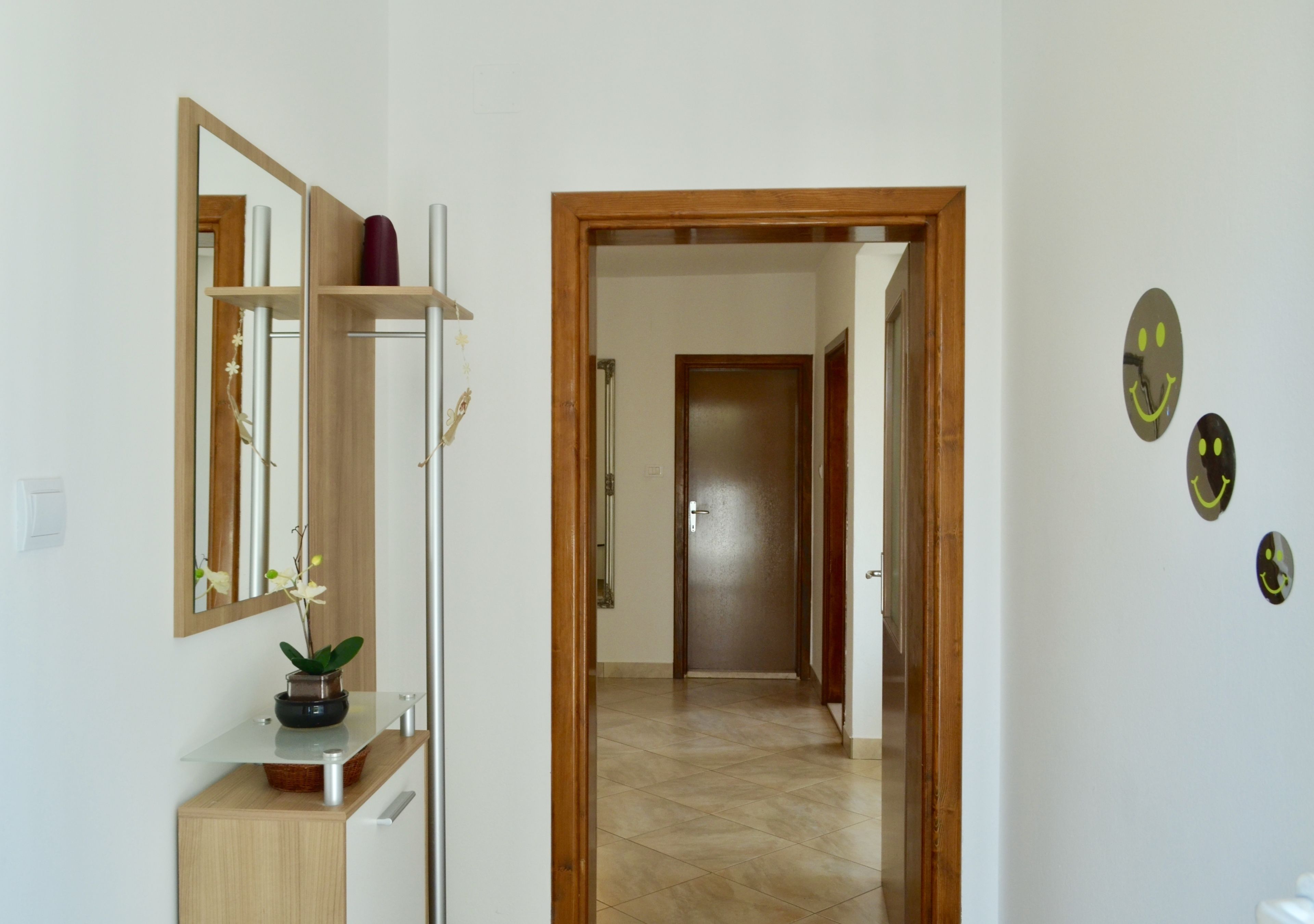 A hallway with a wooden door, a mirror, and a potted plant on a wooden cabinet.