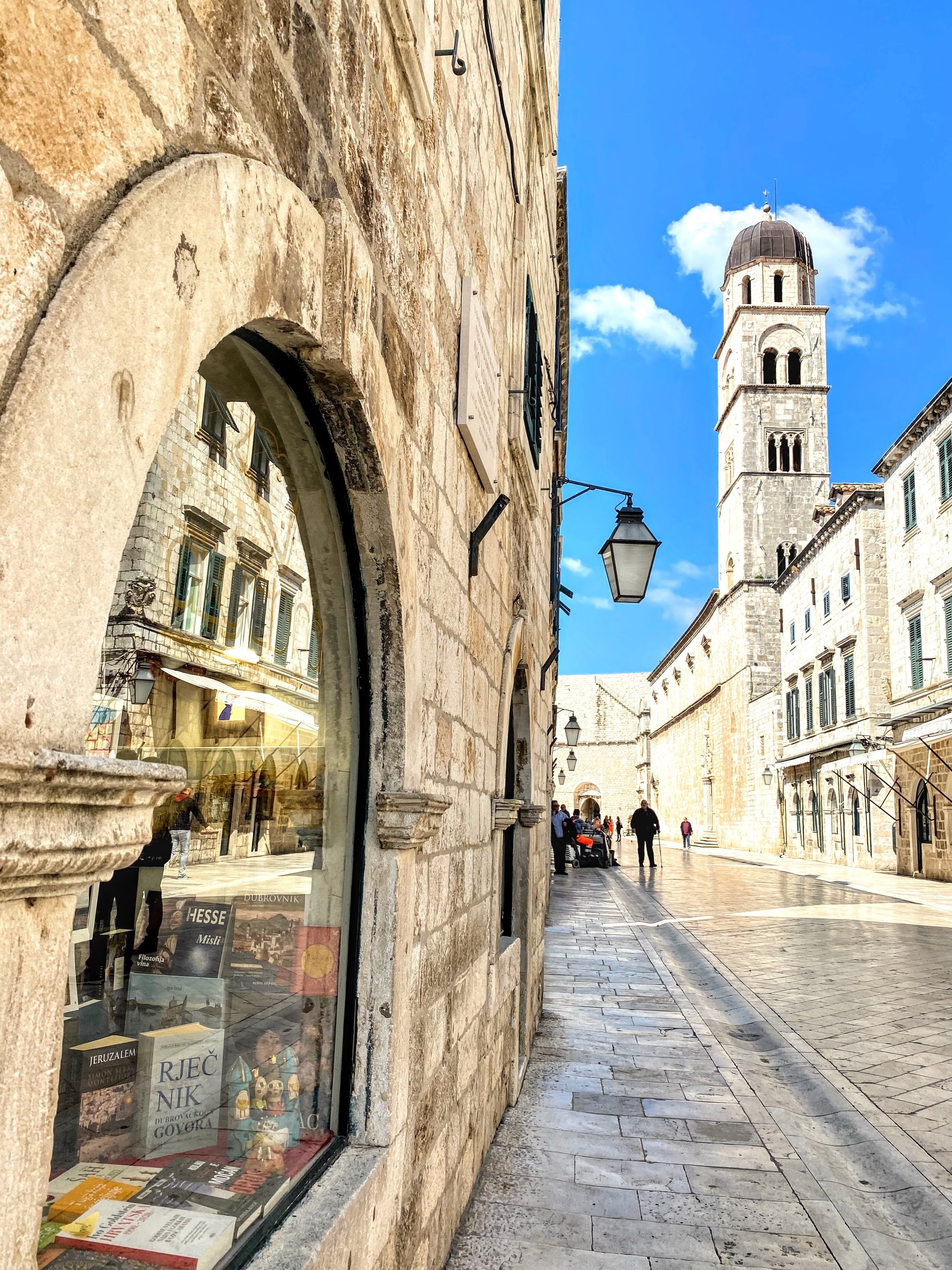 Una calle histórica con edificios de piedra, una torre destacada y un escaparate lleno de libros.