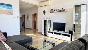 Ein modernes Wohnzimmer mit einer Couch, einem Glastisch, einem Flachbildfernseher und einem Bücherregal.