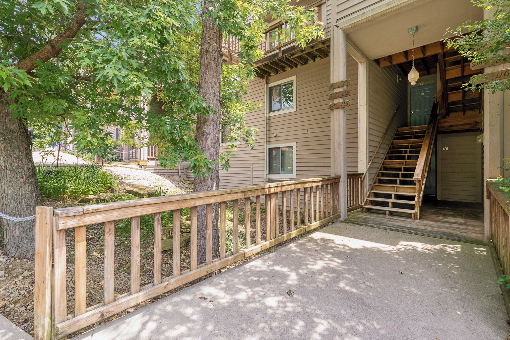 A wooden deck with a railing, a staircase leading to an upper level, and a door with a number '116' visible.