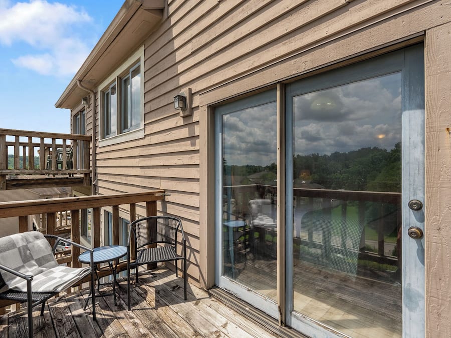 Una terraza de madera con mobiliario exterior, una puerta corrediza de vidrio y vista al paisaje.