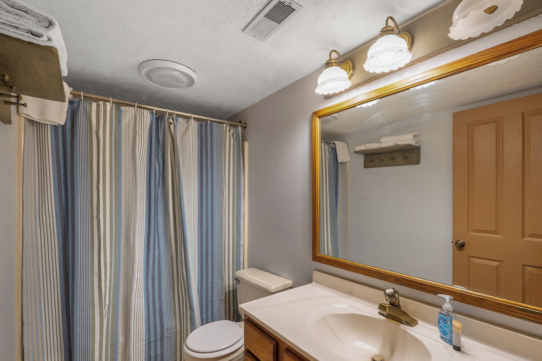 Une salle de bain avec un rideau de douche à rayures, des toilettes, un lavabo avec un miroir et un porte-serviettes.