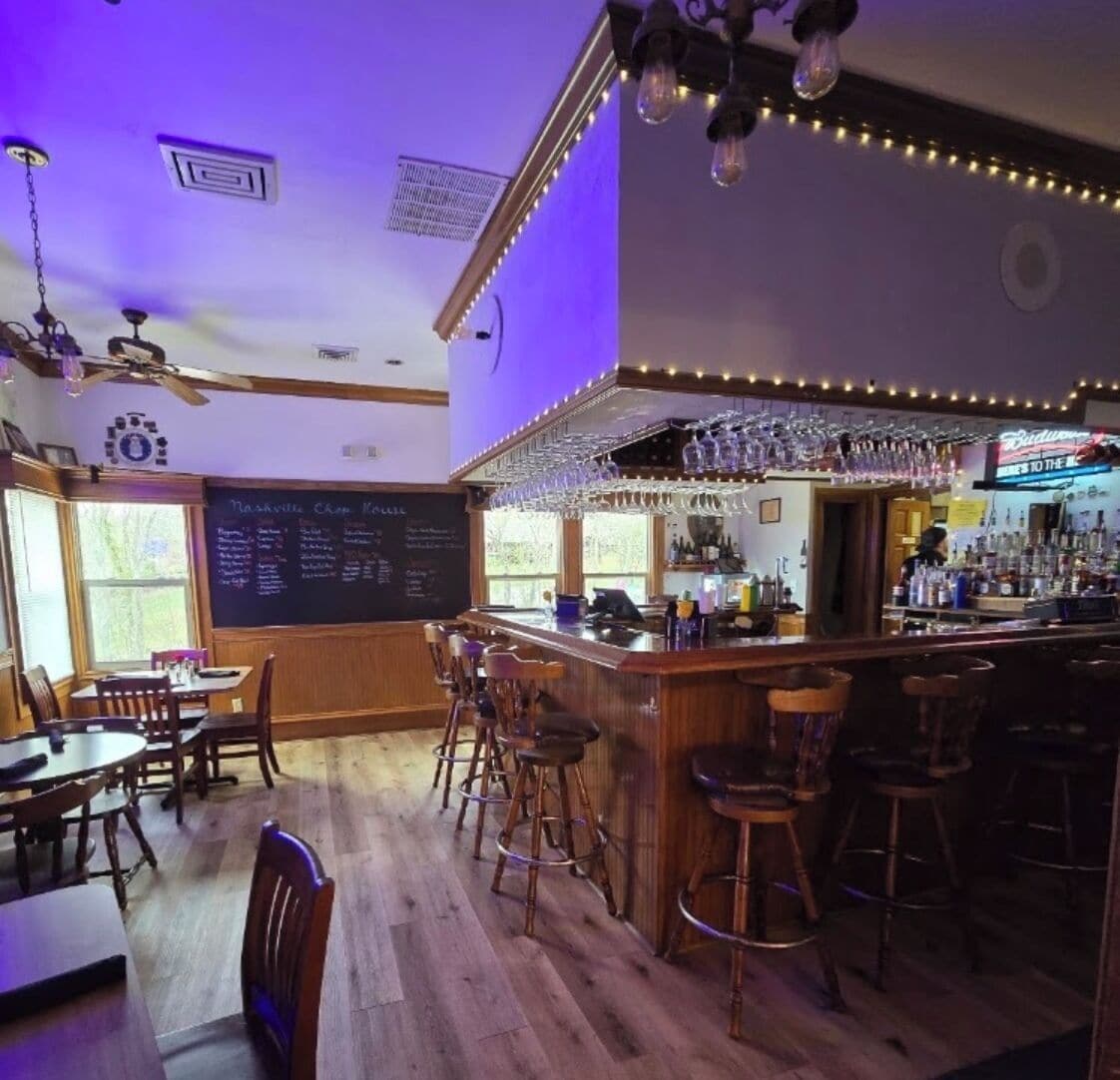 A bar area with wooden flooring, bar stools, a chalkboard menu, and a bar counter with glasses and bottles.