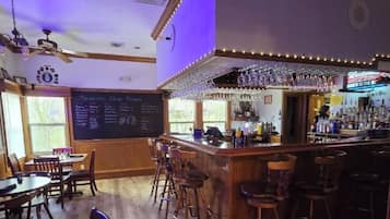 A bar area with wooden flooring, bar stools, a chalkboard menu, and a bar counter with glasses and bottles.