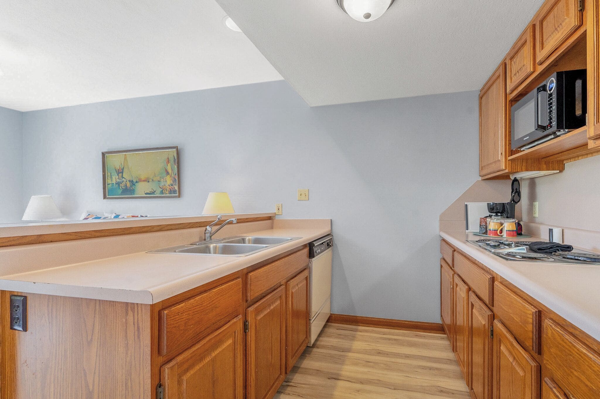 A compact kitchen with wooden cabinets, a stainless steel sink, a microwave, and a small countertop area.