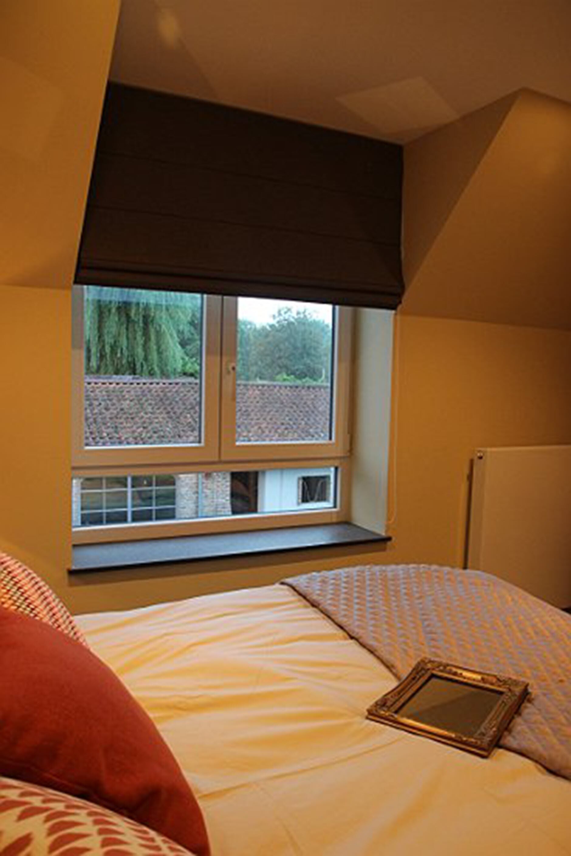 Une chambre à coucher avec un lit, une fenêtre et un cadre photo posé sur le lit.