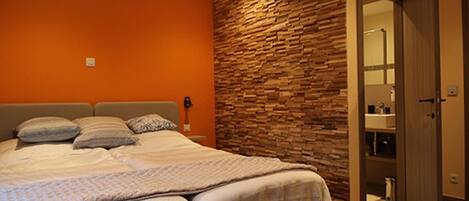 A bedroom with a bed, a stone wall, and a bathroom visible through an open door.