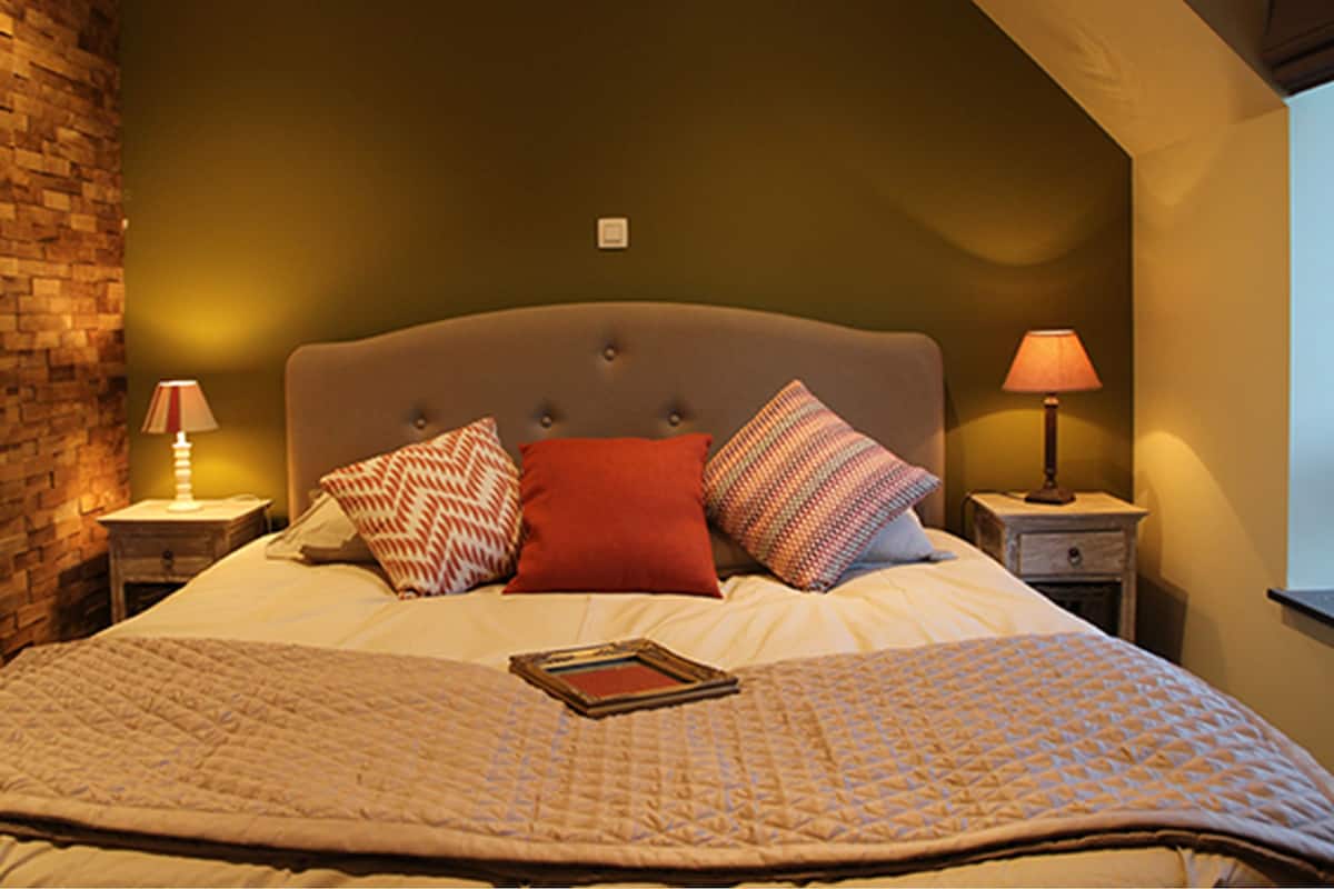 A neatly made bed with a quilt, two pillows, and a bedside lamp on a nightstand.