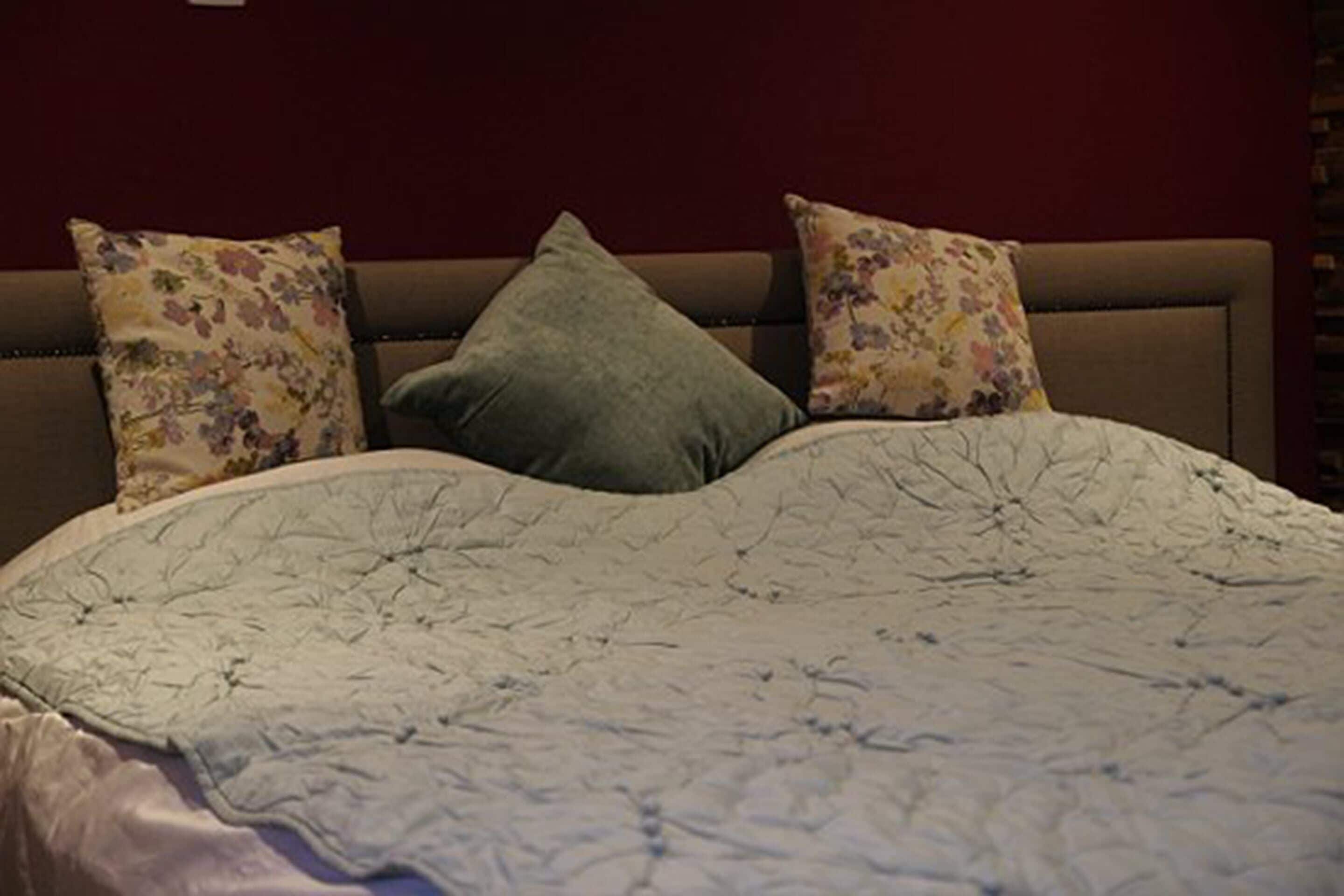 A bed with a floral-patterned pillow and a plain pillow, set against a dark wall.