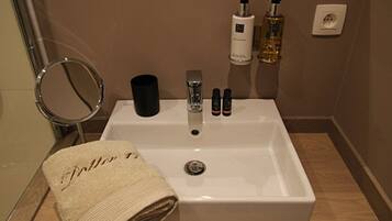 Un baño con un lavamanos blanco, un espejo redondo y una toalla con texto. Hay dos botellas y un recipiente negro sobre el lavamanos.