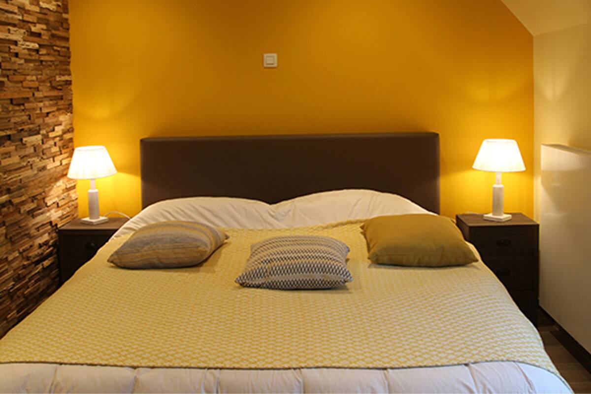 A neatly made bed with a patterned bedspread, two bedside lamps, and a brick accent wall.