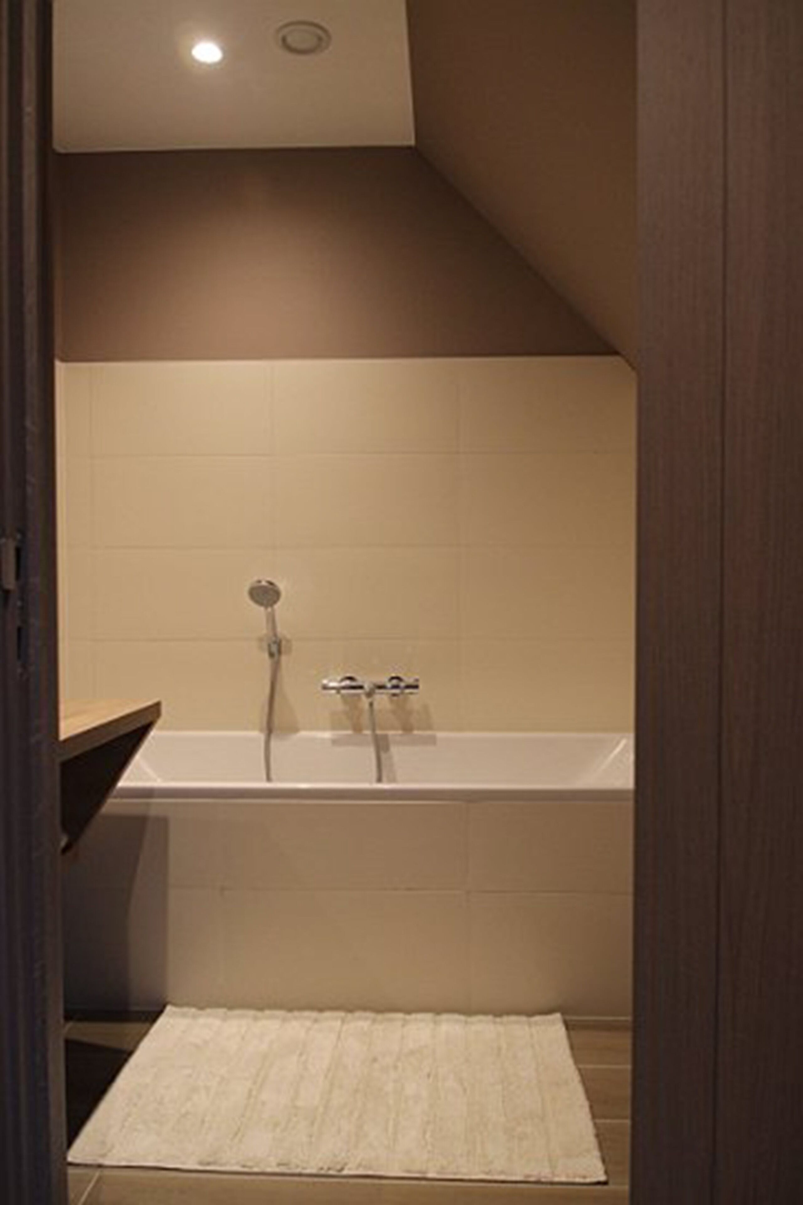 Une salle de bain avec une baignoire, une douche et un tapis blanc sur le sol.