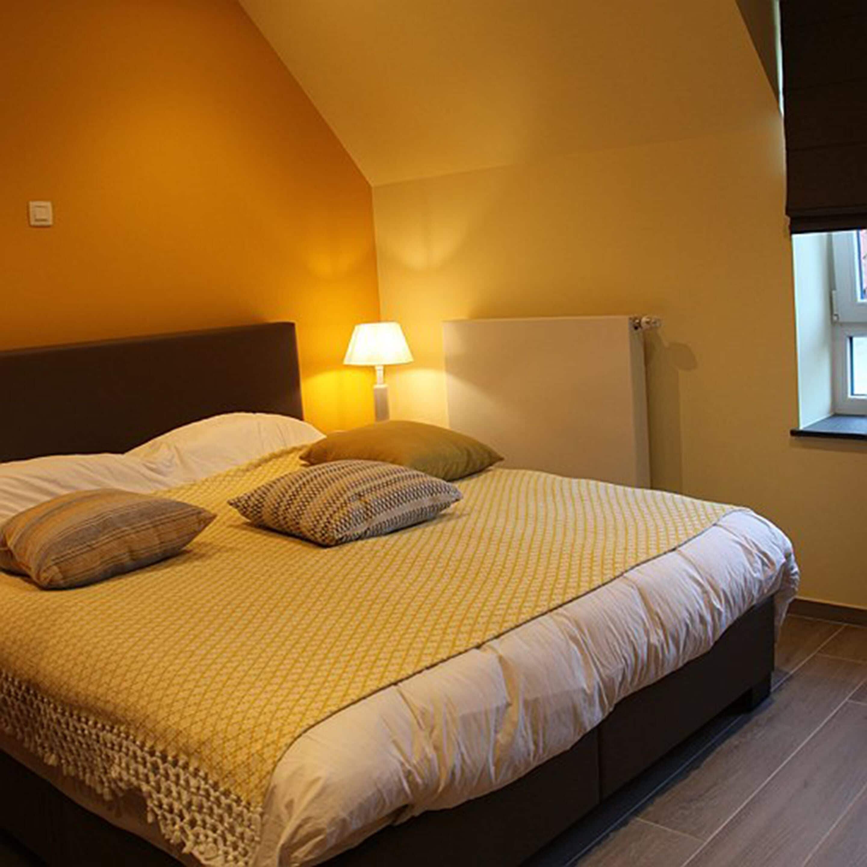 Un dormitorio con cama, almohadas, lámpara y ventana.