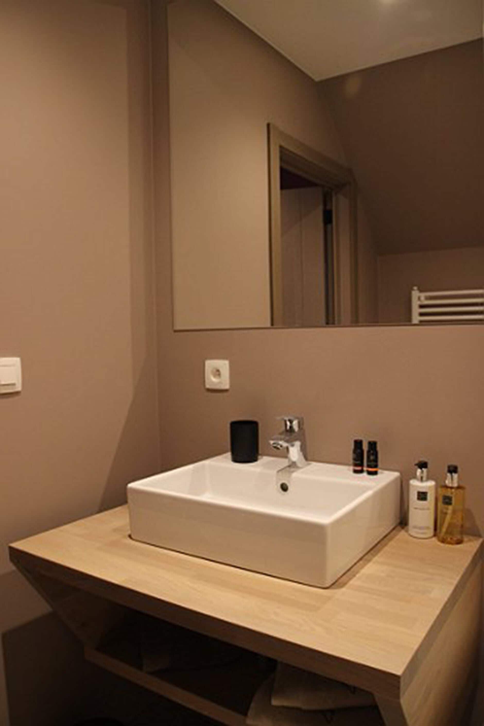 A modern bathroom with a large mirror, a white sink, and a wooden vanity.