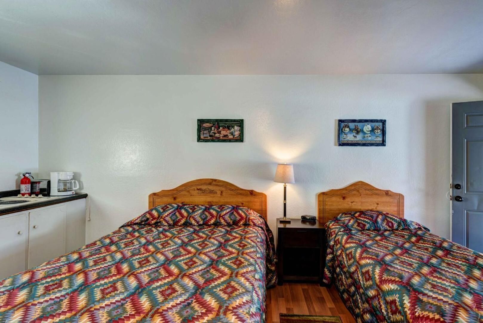 A room with two beds, a nightstand, a lamp, a coffee maker, and a fire extinguisher.
