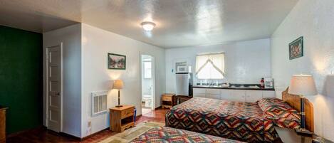 A bedroom with two beds, a kitchenette, a bathroom, and a small living area.