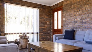A cozy living room with a brick wall, a wooden coffee table, a sofa, and a window with blinds. - Leawarra stays in the farm - Fleurieu Peninsula (Pages Flat)