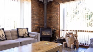 A cozy living room with a sofa, a wooden coffee table, a fireplace, and a view of the outdoors through large windows. - Leawarra stays in the farm - Fleurieu Peninsula (Pages Flat)