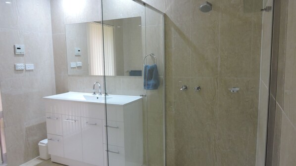 Un baño moderno con ducha envuelta en vidrio, tocador blanco con cajones y un espejo sobre el lavabo.