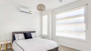 A modern bedroom with a large bed, a standing lamp, an air conditioning unit, and a view through floor-to-ceiling windows. - Diamond Bay Beach House (SORRENTO)