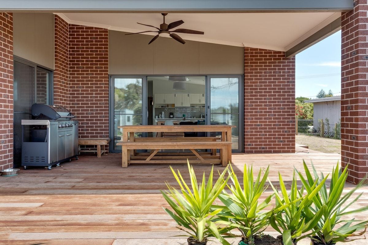 A covered outdoor area with a barbecue grill, a wooden table, and potted plants.