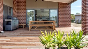 A covered outdoor area with a barbecue grill, a wooden table, and potted plants. - Diamond Bay Beach House (SORRENTO)