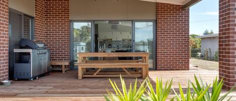 A covered outdoor area with a barbecue grill, a wooden table, and potted plants.