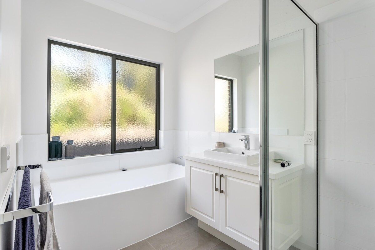 A modern bathroom with a bathtub, a glass shower enclosure, and a large window with frosted glass.