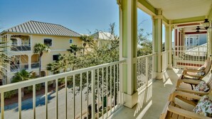A balcony with a view of a building, a street, and some greenery.