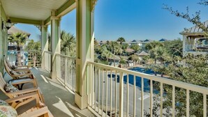 A covered balcony with lounge chairs, a pool, and a view of other buildings and trees. - 🏝️ Seaside Therapy| 6BR | Near Resort Pool and Beach! (Destin)