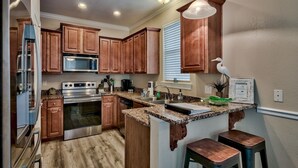 A kitchen with wooden cabinets, stainless steel appliances, granite countertops, and a built-in island with stools. - 🏝️ Seaside Therapy| 6BR | Near Resort Pool and Beach! (Destin)