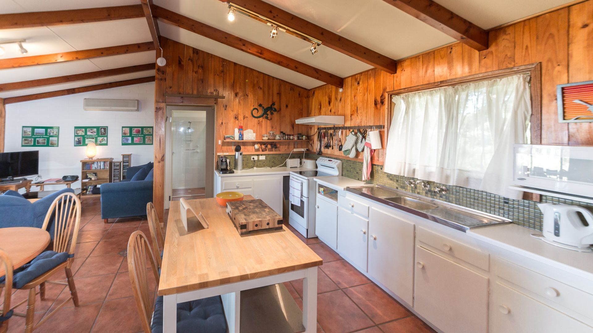 A cozy kitchen with wooden walls, a dining area with a table and chairs, and a living room with a sofa and TV.