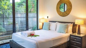 Habitación de hotel con una cama grande, dos lámparas de noche, un espejo redondo y vistas al verdor por la ventana.
