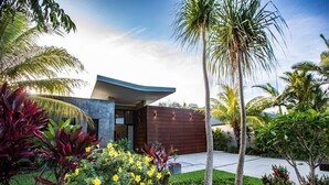 Una casa moderna con techo curvo, rodeada de plantas tropicales y palmeras.