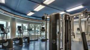 Un gimnasio con diversos equipos de ejercicio, ventanas amplias y techo azul.