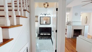 A hallway leading to a bathroom with a black vanity, a mirror, and a chandelier.