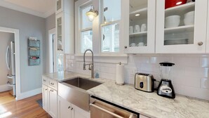 A modern kitchen with white cabinetry, a stainless steel sink, a built-in oven, a toaster, and a blender.