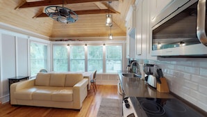 A modern kitchen with a built-in stove, a dining area with a sofa, and large windows offering a view of the outdoors.