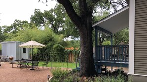 A covered patio with a table and chairs, a barbecue grill, and a shed in a garden setting. - 100-year old bungalow in the heart of the City, walking distance to Zilker Park! (Austin)