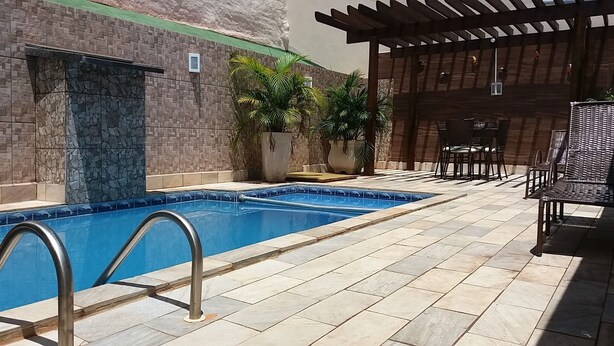 Une piscine bordée d’un mur en pierre et dotée d’une terrasse carrelée, entourée de plantes en pot et de mobilier d’extérieur.