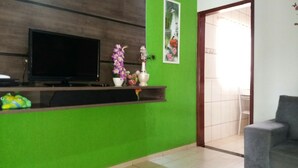 Un espace d’accueil agrémenté d’un mur végétal, d’un téléviseur à écran plat, d’une petite étagère avec des objets décoratifs et d’un fauteuil gris.