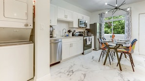 Une cuisine moderne avec des meubles blancs, un four encastré et un coin repas comprenant une table et des chaises.