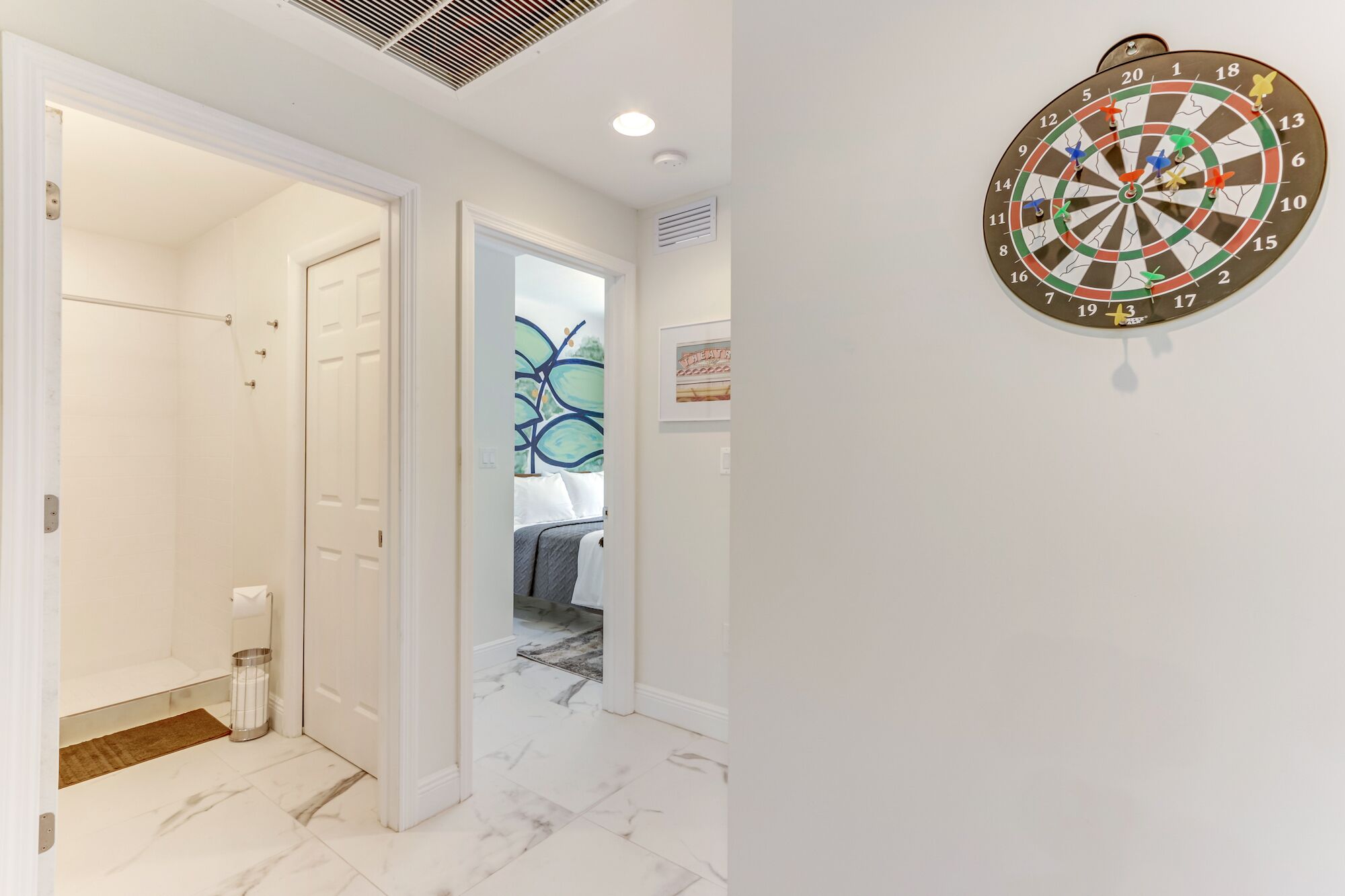 Ein Flur mit Dartscheibe an der Wand, einer Tür zu einem Badezimmer und einer Treppe.