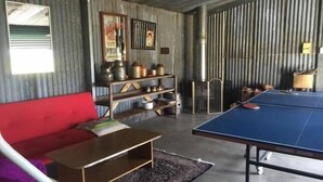 A room with a red sofa, a ping pong table, and shelves with various items. - Pizza oven; fire pit; lots of space indoor and outdoor, fires and aircon. Groups (Mudgee)