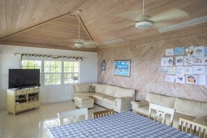 Une pièce avec un plafond en bois, une télévision, un canapé, une table à manger et un mur décoré de dessins d’enfants.