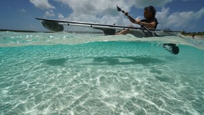 Eine Person paddelt mit einem Kajak in klarem türkisblauem Wasser, mit Blick auf den Himmel und entferntes Land.